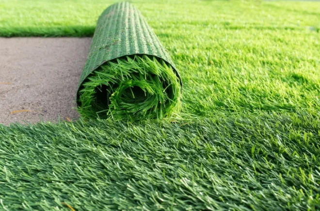 Rollo de pasto sintético verde parcialmente extendido sobre una superficie de césped