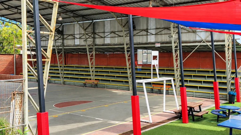 Pilares metálicos con protectores rojos que sostienen los toldos del patio de Denver School