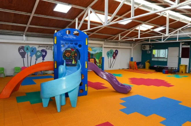 Patio de párvulos techado con resbalines de colores y piso modular amarillo con figuras azules, verdes y rosadas